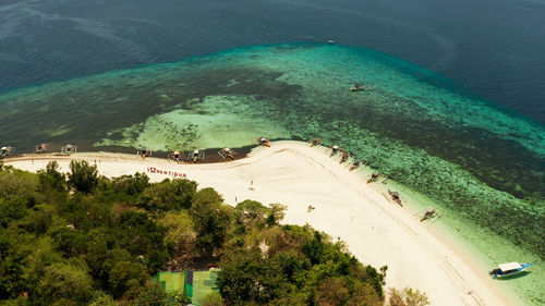 Tropical island and sandy beach surrounded by atoll coral reef and blue sea. 