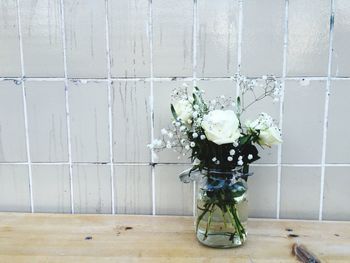 White flowers in vase on table by wall