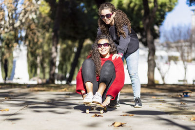 Playful female friends enjoying with skateboard outdoors