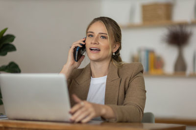 Woman working at home with laptop and speaking on mobile phone. home office. gray notebook 