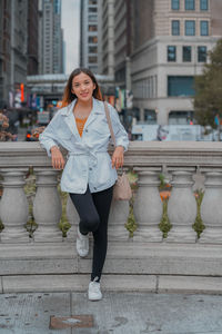 Portrait of smiling young woman sitting on footpath in city