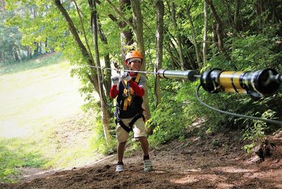 Full length of boy holding cable while zip lining at forest