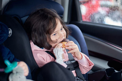 Siblings in car seats having snacks in the back seat of a car on a rainy day