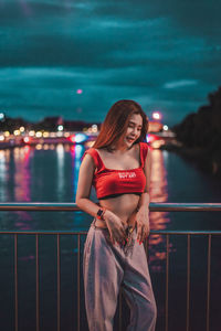 Smiling young woman standing on bridge over river at night