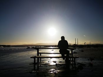 Rear view of man standing at beach against sky during sunset