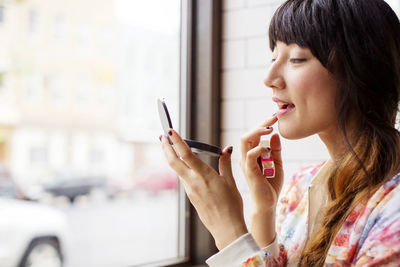 Woman applying lipstick while sitting in bar