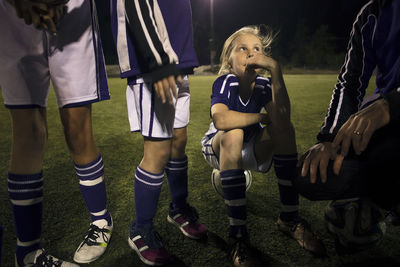 Girl looking at coach explaining strategy on soccer field at night