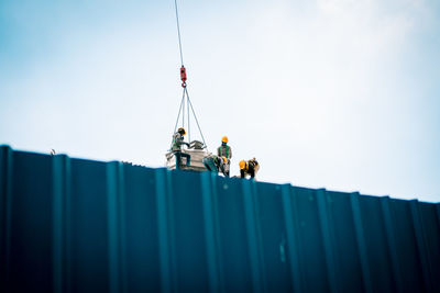 Low angle view of people working on cargo container against sky