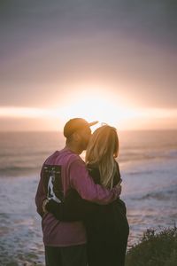 Rear view of couple standing at beach during sunset