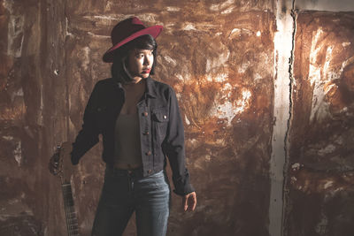 Young guitarist standing against wall