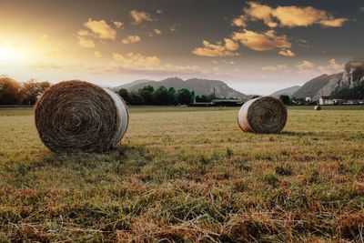 Hay bales on field against sky during sunset