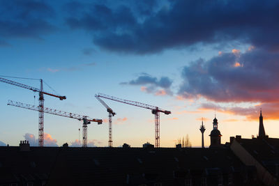 Silhouette cranes and rheinturm against cloudy sky at sunset