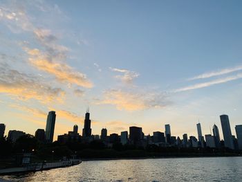 Sea by modern buildings against sky during sunset