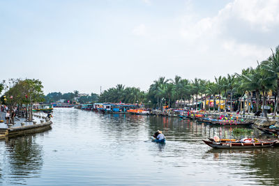 People rowing rowboat in river against sky