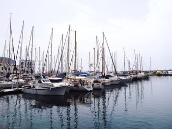 Sailboats moored at harbor against sky