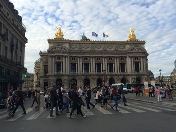 Tourists in front of building against cloudy sky
