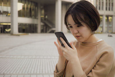 Smiling woman using mobile phone while standing in city