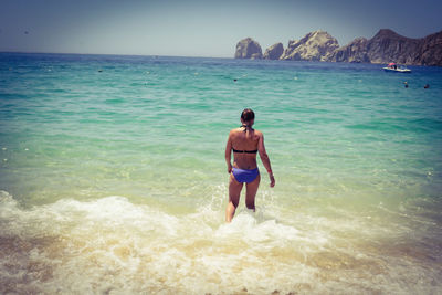 Rear view of sensuous woman in bikini walking on beach