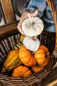 Cropped image of hand holding pumpkins over vegetable basket