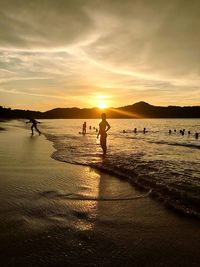 Silhouette people standing on beach against sky during sunset