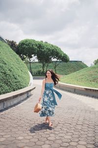 Smiling woman holding bag while walking on footpath