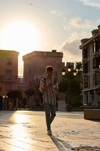 A young man with afro hair walks at sunset while using his cell phone