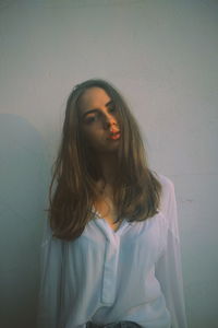 Portrait of young woman standing by white wall