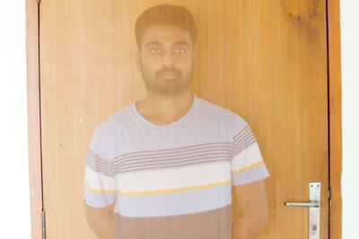 Portrait of young man standing against door at home