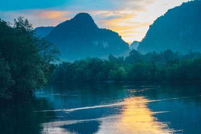 Scenic view of lake by trees against sky during sunset