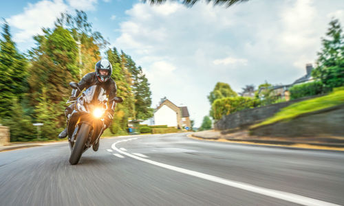 Blurred motion of man riding motorcycle on road against cloudy sky