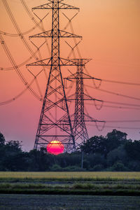 Electricity pylon substation in farmland with big red sunset for technology background