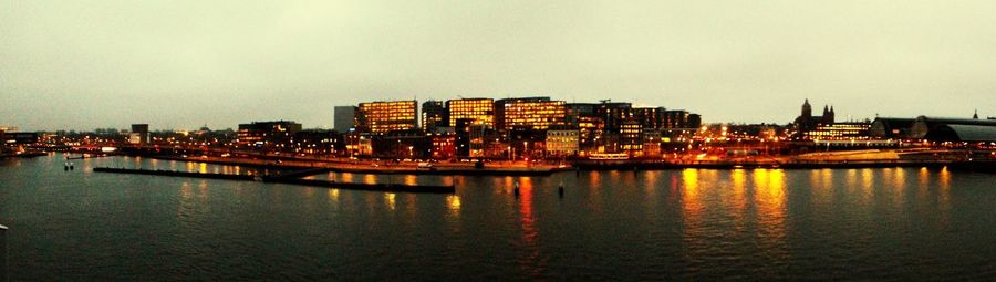 Illuminated cityscape by river against sky at night