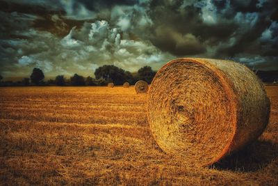 Hay bales on field against cloudy sky