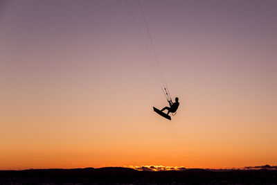 Silhouette person wakeboarding against sky during sunset