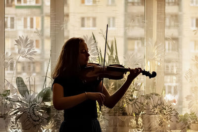 Young woman playing violin by window