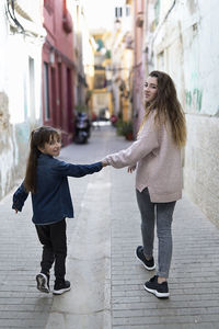 Rear view of sisters holding hands while walking in alley