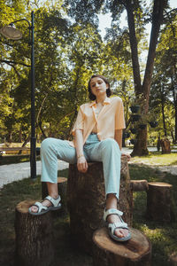 Portrait of smiling young woman sitting on tree trunk at park