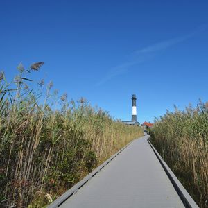 Lighthouse amidst field against clear blue sky