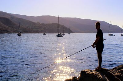 Silhouette mature man fishing by sea against mountains