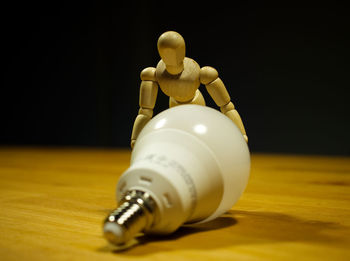 Close-up of figurine with led bulb on table against black background