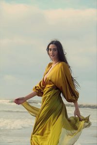 Young woman in yellow dress standing against  sky