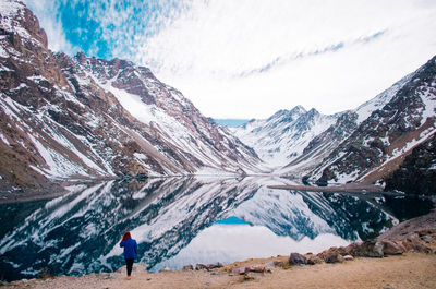 Rear view of young woman standing by lake against mountain range