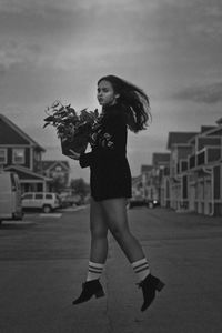 Young woman holding potted plant while jumping on road in city