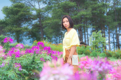 Woman standing by flowering plants against trees