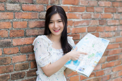 Portrait of smiling woman standing against brick wall