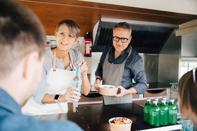 Mature owners serving food and drink to customers while standing in commercial land vehicle