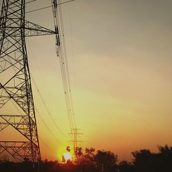 Low angle view of electricity pylon against sky during sunset