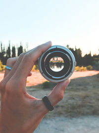 Close-up of hand holding lens against sky