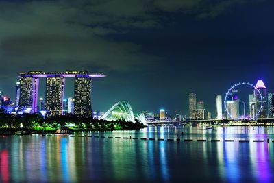 Illuminated buildings by river in city against sky at night