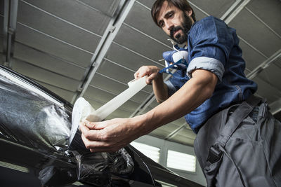 Man taping side-view mirror of car in factory